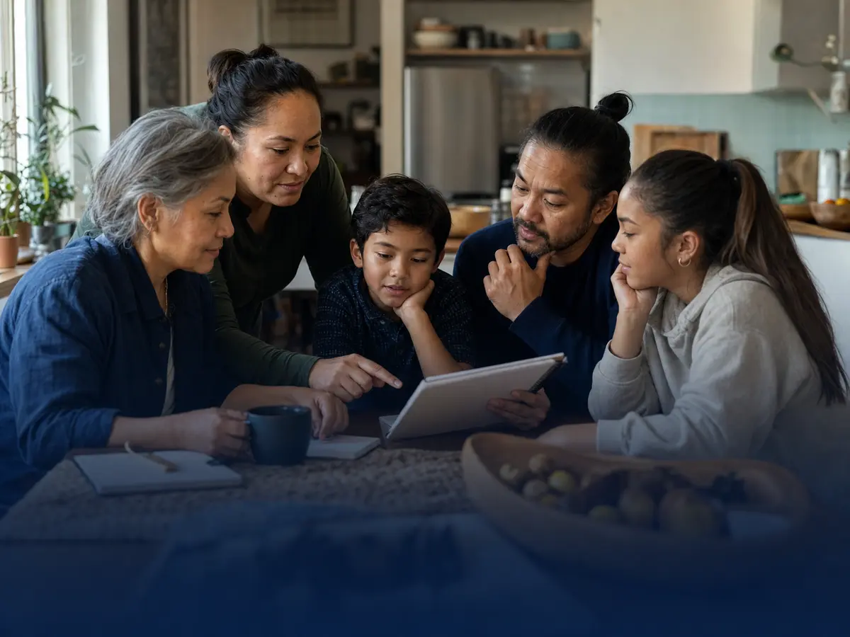 A multigenerational family gathered around a table, reviewing practical information together on a tablet.